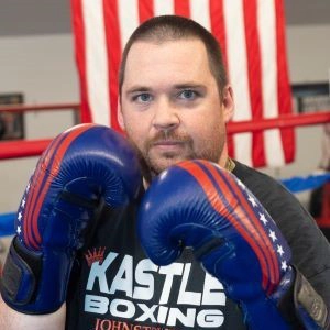 Patrick in a boxing ring wearing blue boxing gloves